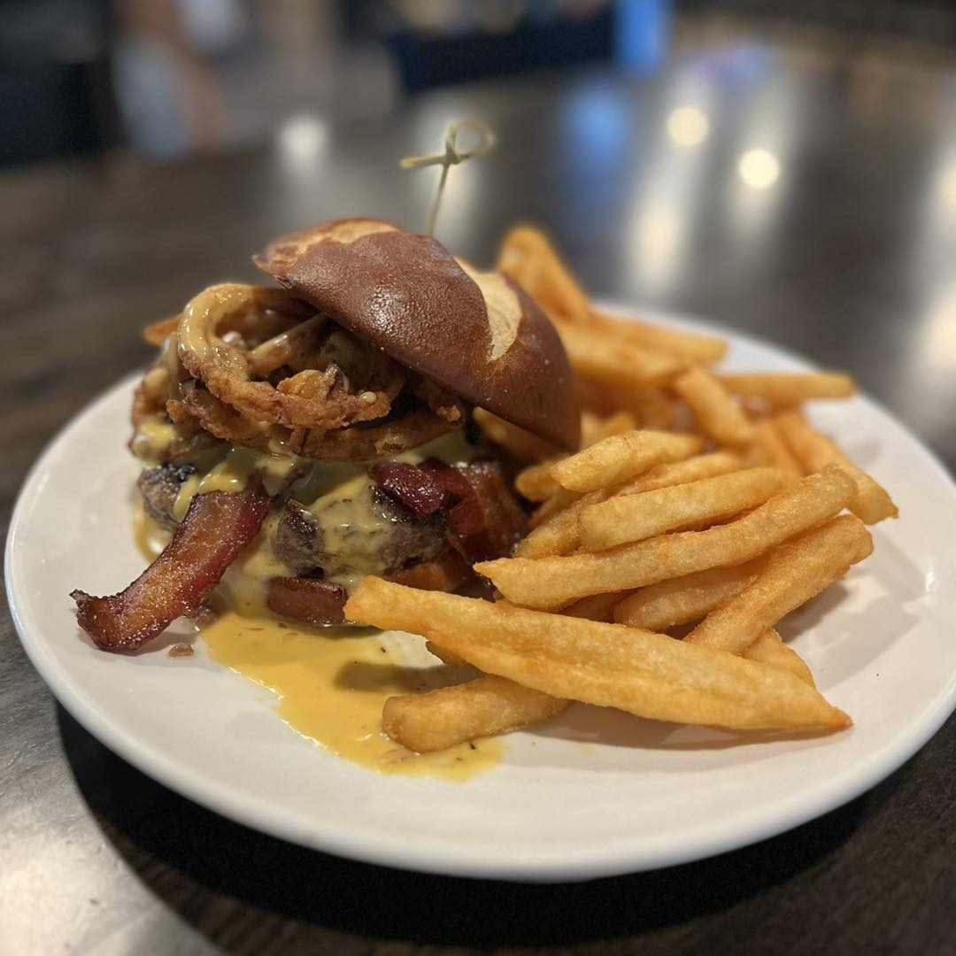 Loaded burger with onion straws and bacon on a pretzel bun with fries